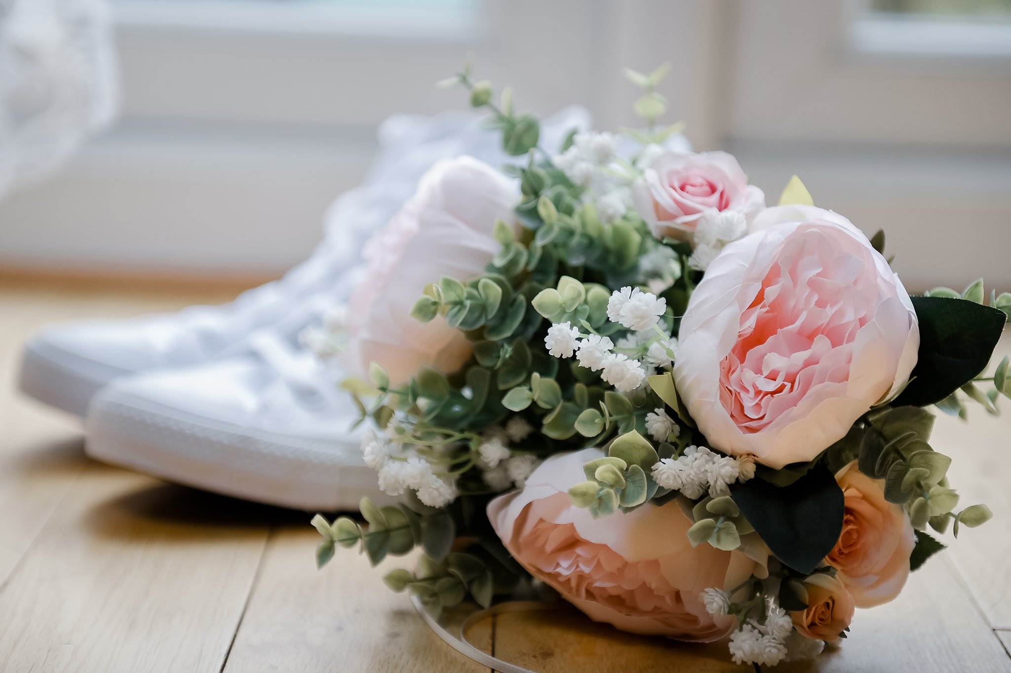 White Converse wedding trainers and brides matching flower bouquet, placed on natural timber floorboards